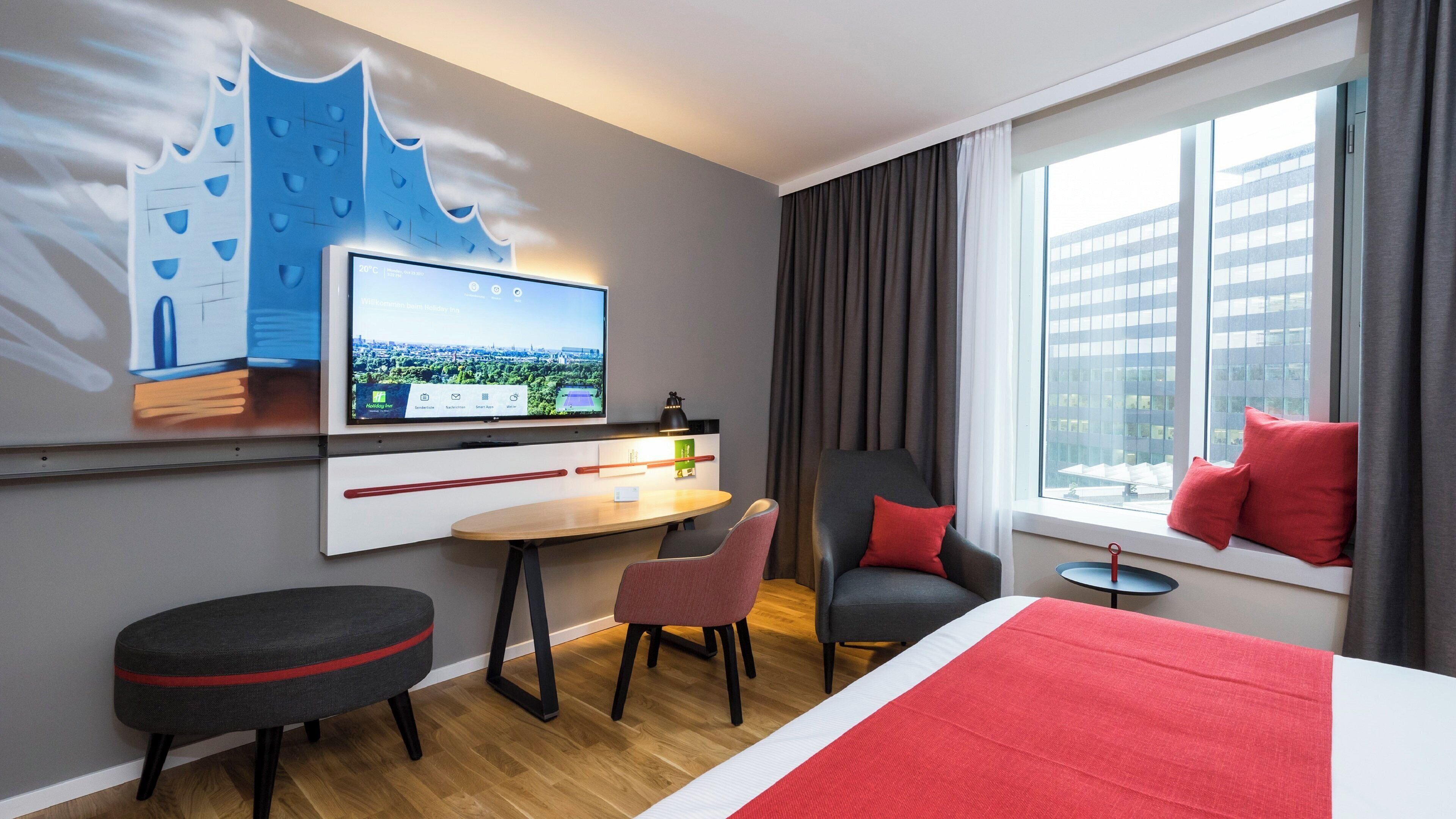 Une chambre d’hôtel avec un lit, un bureau, une chaise, une télévision et une fenêtre avec des rideaux.