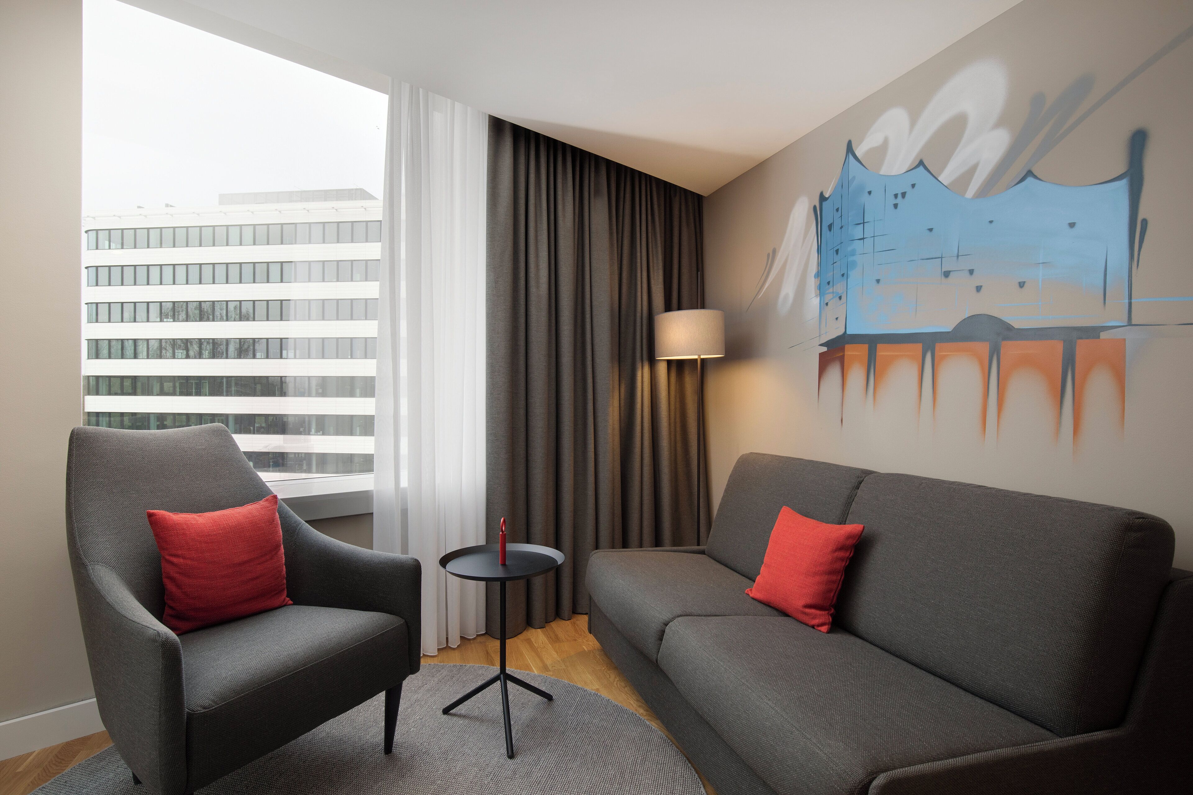 Una camera d'hotel moderna con un divano grigio, una poltrona abbinata e un piccolo tavolino.