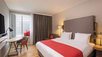 Habitación de hotel con cama, escritorio, silla, televisor y ventana con cortinas.