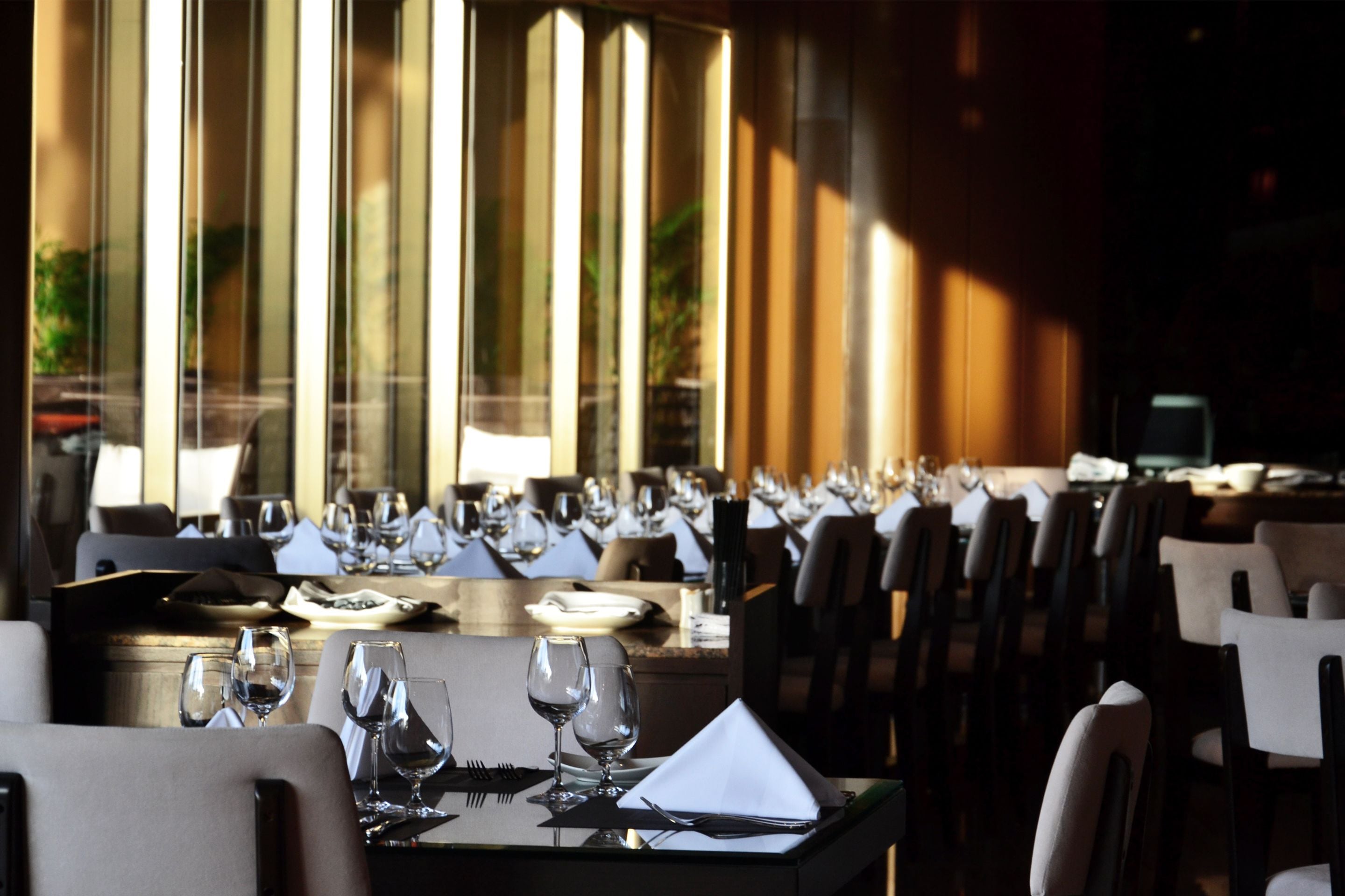 A restaurant with long tables set for dining, large windows, and a warm interior lighting.