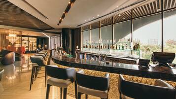 Un área de bar moderna con una barra larga, taburetes y vistas de la ciudad a través de amplias ventanas.
