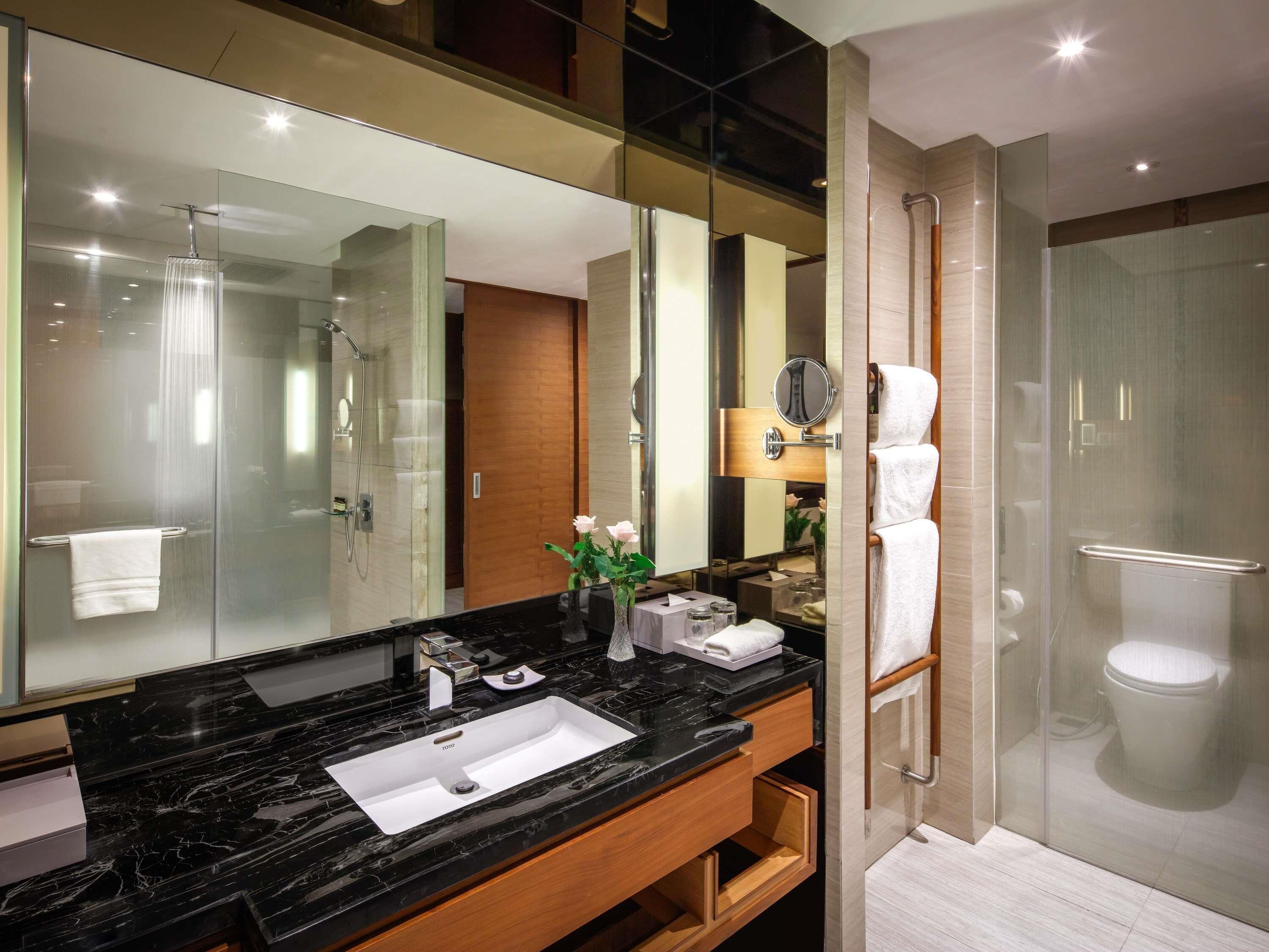 A modern bathroom with a black marble sink, a large mirror, a glass shower enclosure, and a wooden vanity.