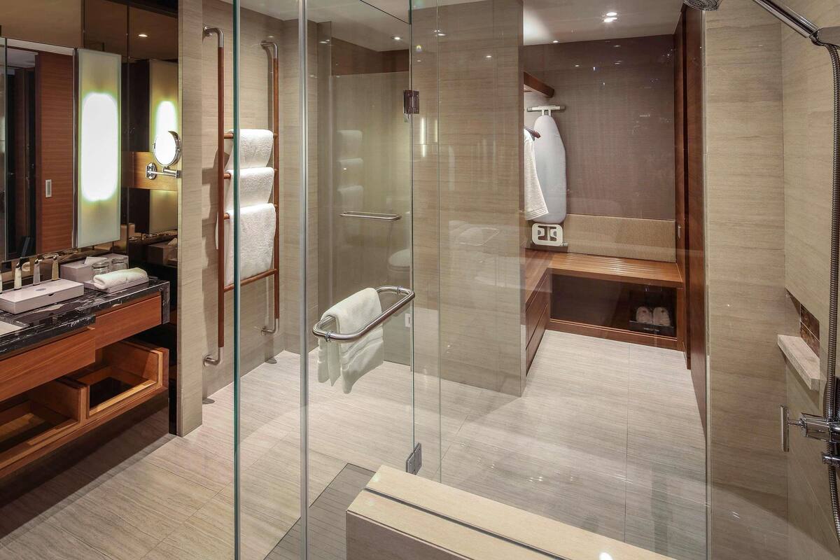 A modern bathroom with a glass-enclosed shower, a vanity with a marble countertop, and a wooden bench.
