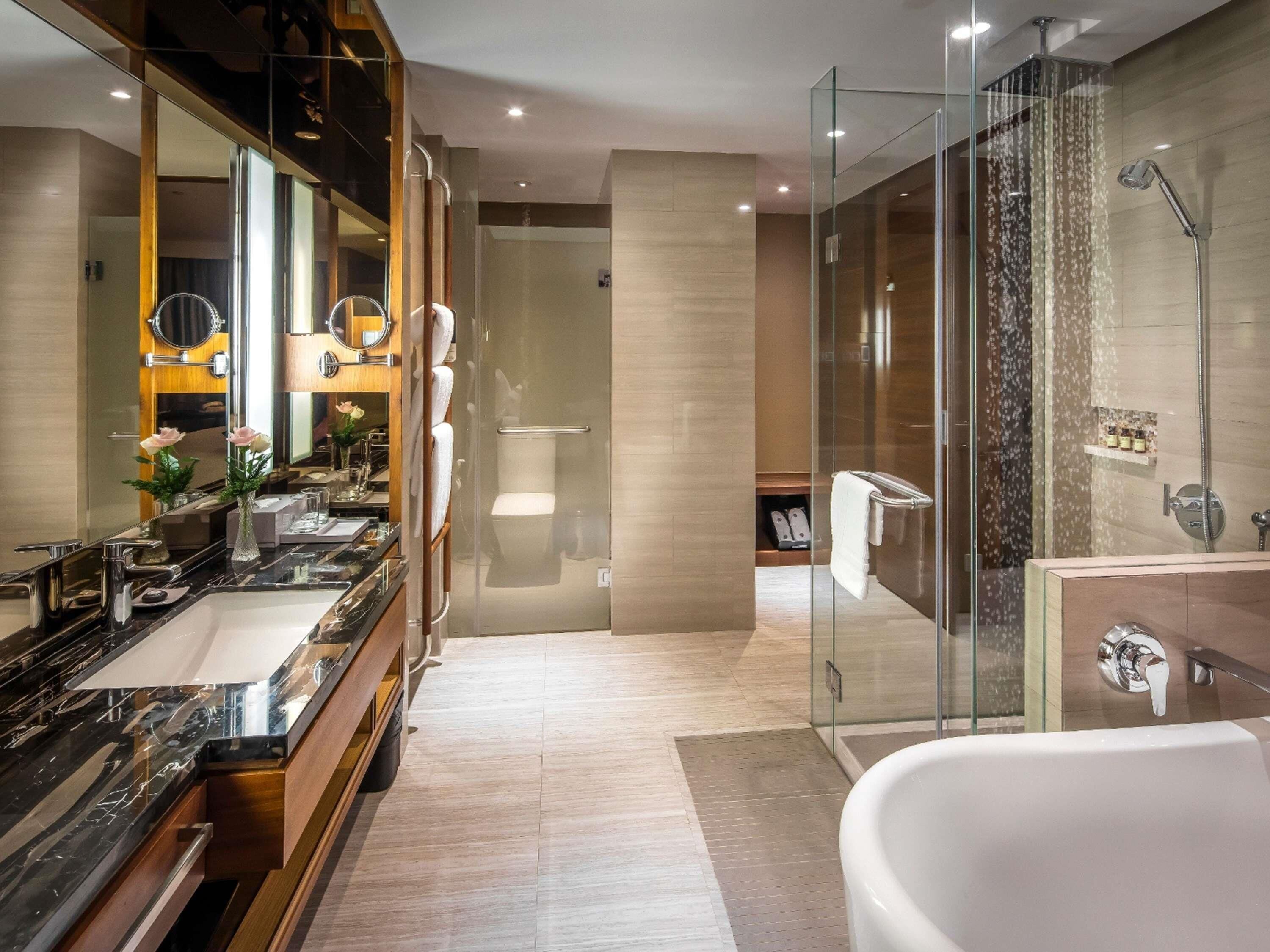 A modern bathroom with a large mirror, a bathtub, a glass-enclosed shower, and a vanity with a marble countertop.