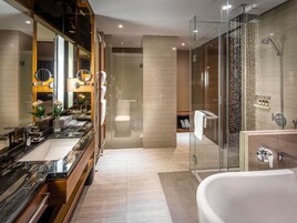 A modern bathroom with a large mirror, a bathtub, a glass-enclosed shower, and a vanity with a marble countertop.