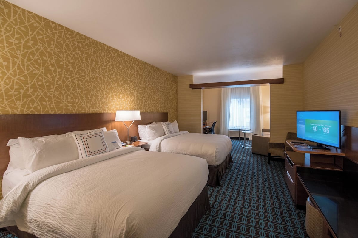 A hotel room with two beds, a TV, a desk, and a patterned carpet.