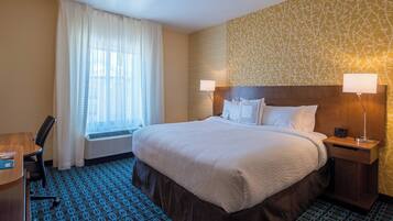 A hotel room with a large bed, two bedside tables with lamps, a desk, a chair, a window with curtains, and a patterned wall.