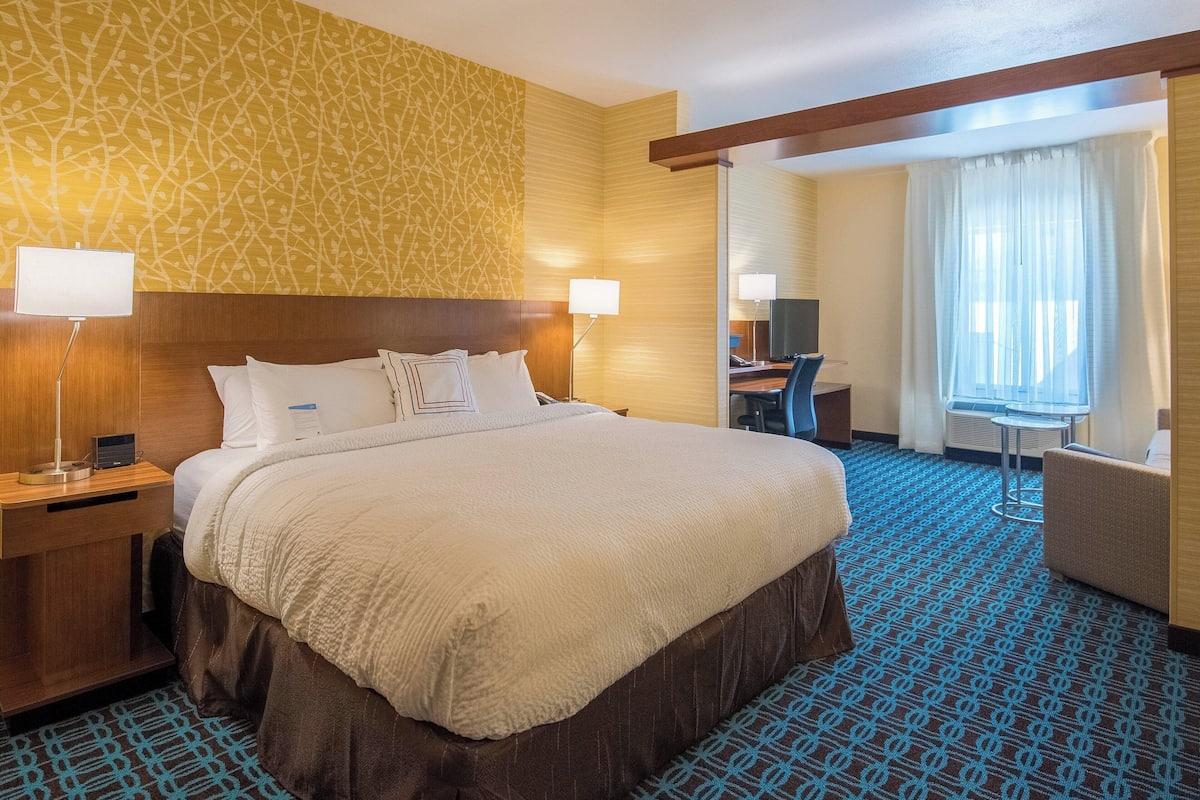 A hotel room with a large bed, a desk, a chair, and a small table.
