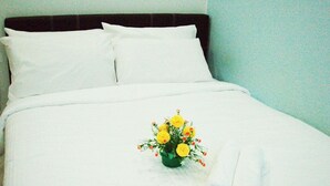 A neatly made bed with white linens, a rolled towel, and a small bouquet of yellow flowers. - Garden Vacation Suite (Bentong)