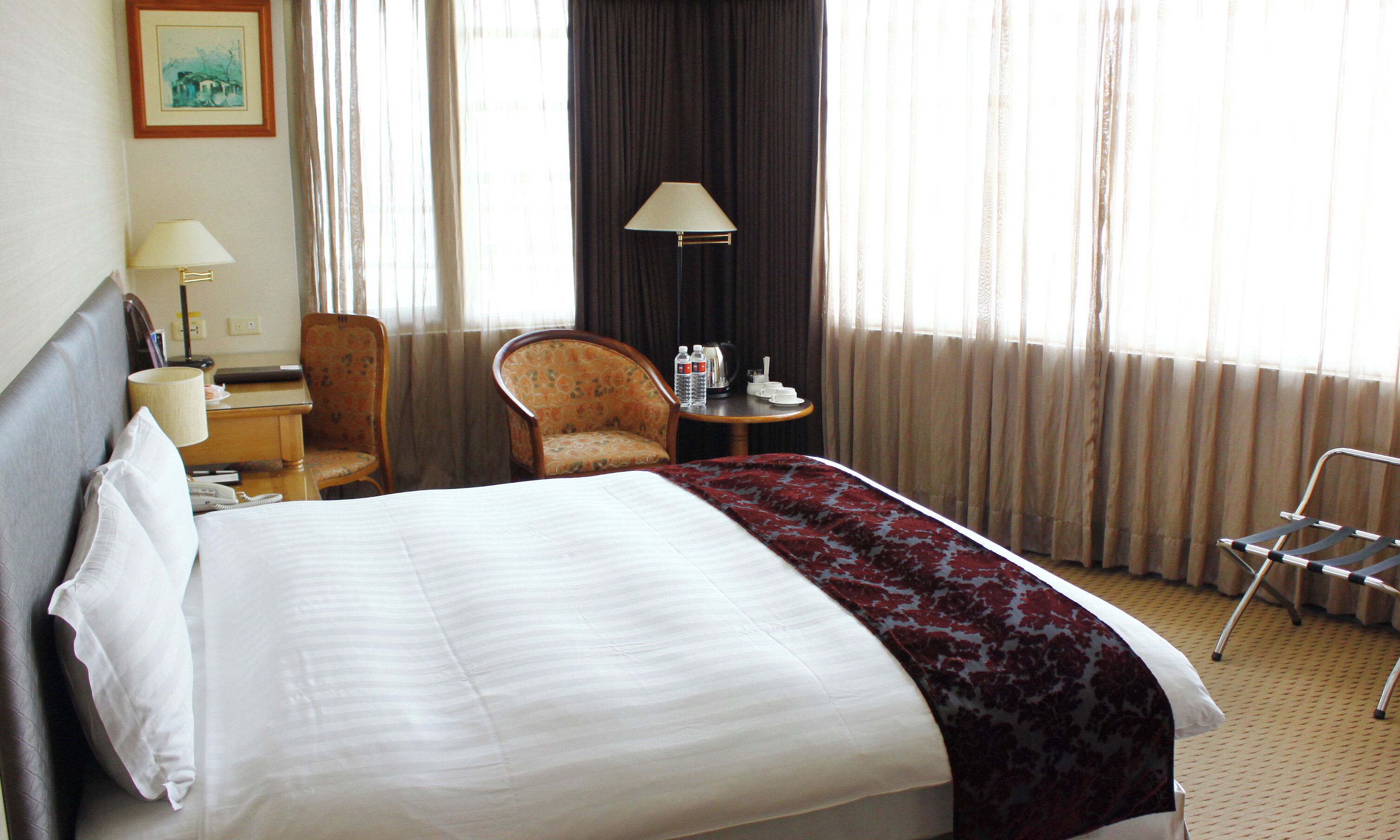A hotel room with a bed, a chair, a table with a lamp, and a window with curtains.