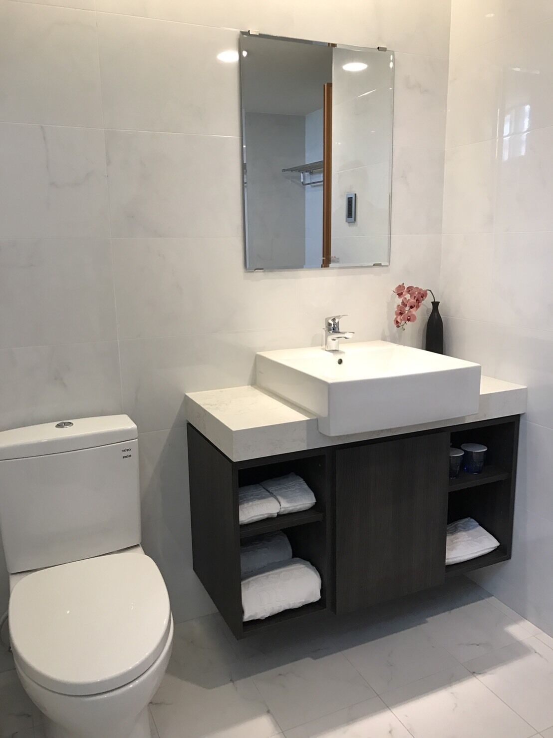 A modern bathroom with a white toilet, a white sink with a dark cabinet, and a mirror above the sink.