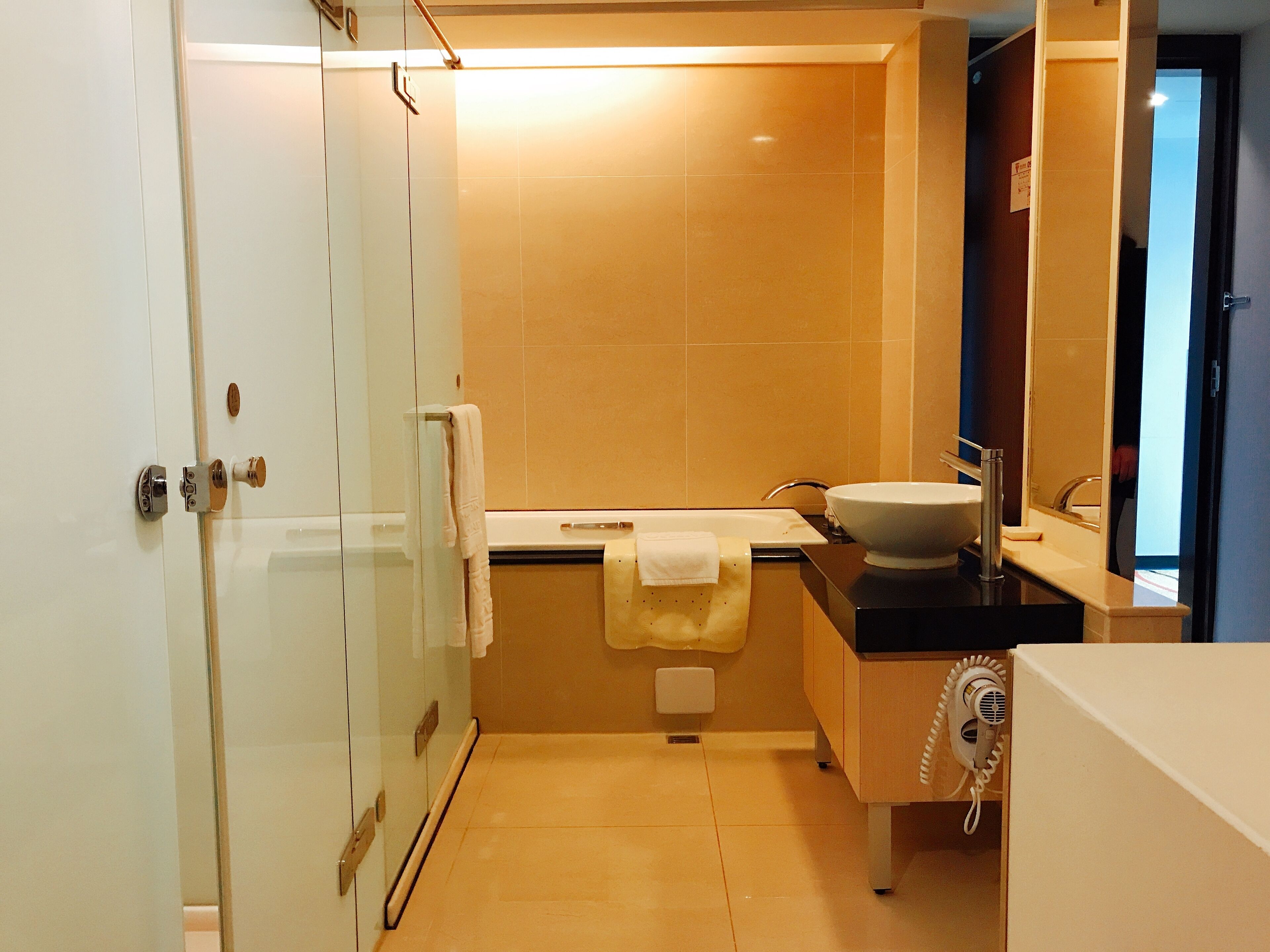 Une salle de bain moderne avec une douche à parois de verre, un lavabo blanc et un sèche-cheveux posé sur un meuble.