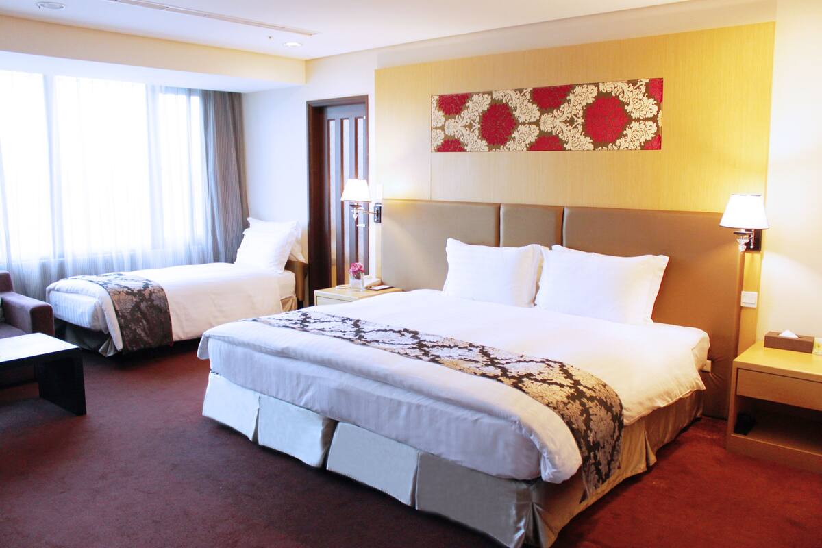 A hotel room with two beds, a sofa, and a desk.