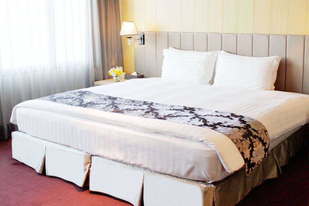 A hotel room with a large bed, a nightstand with a lamp, and a window with curtains.