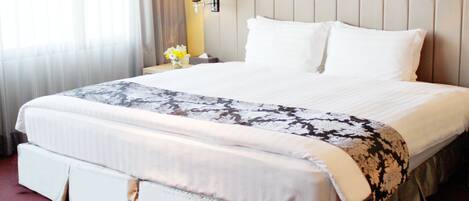 A hotel room with a large bed, a nightstand with a lamp, and a window with curtains.