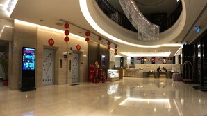 Un moderno vestíbulo de hotel con un directorio digital, ascensores, una recepción y una araña.