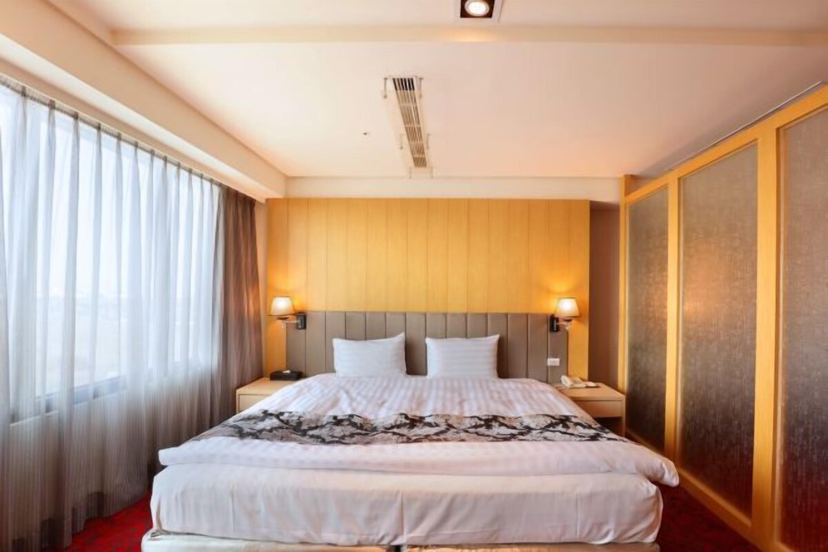 A hotel room with a large bed, two bedside lamps, a wooden headboard, and a red carpet.