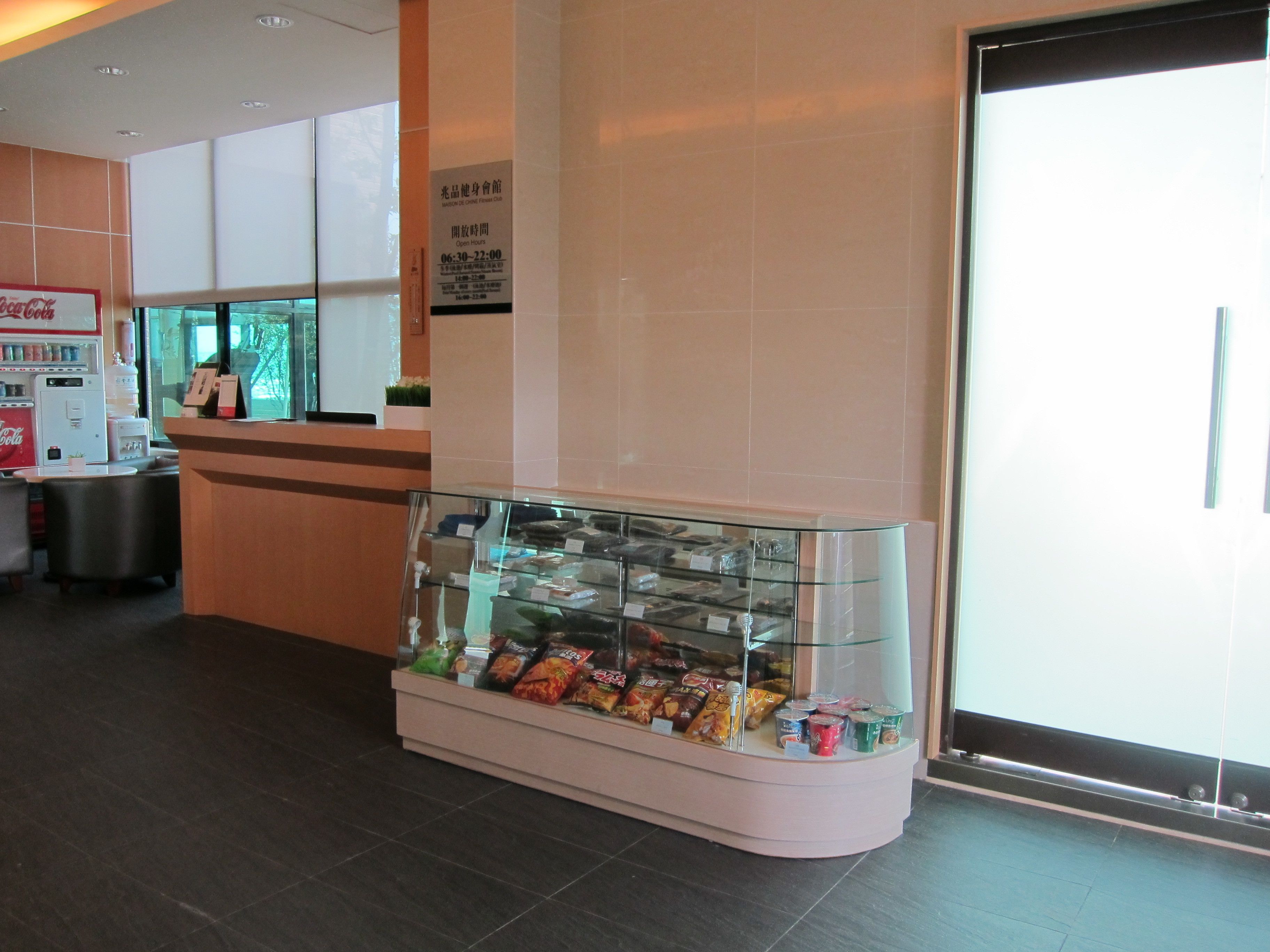 A snack display case in a hotel lobby with a Coca-Cola vending machine and a reception desk.