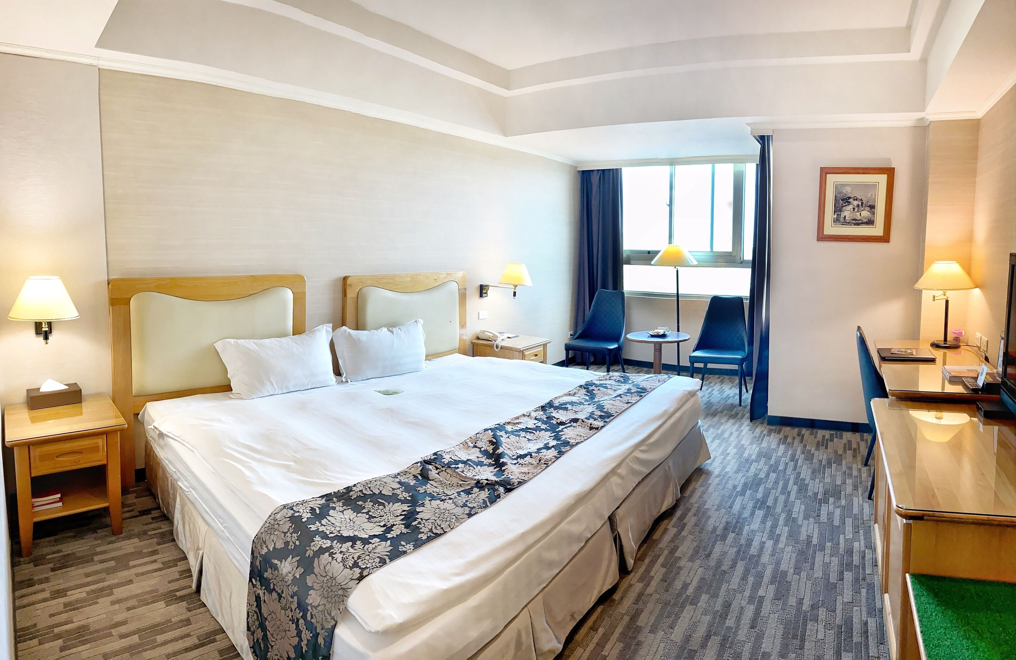 A hotel room with a large bed, two bedside tables with lamps, a desk with a chair, and a small table with a chair.