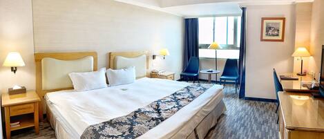 A hotel room with a large bed, two bedside tables with lamps, a desk with a chair, and a small table with a chair.