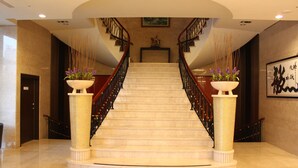 Una imponente escalera con acabado de mármol, flanqueada por dos grandes columnas con plantas.