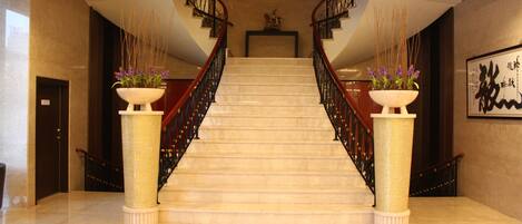 A grand staircase with a marble finish, flanked by two large columns with plants.