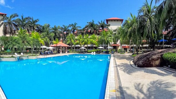 Una gran piscina rodeada de palmeras y un edificio de hotel con varios balcones.