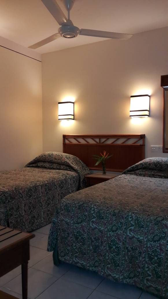 A hotel room with two beds, a ceiling fan, and wall-mounted lights.