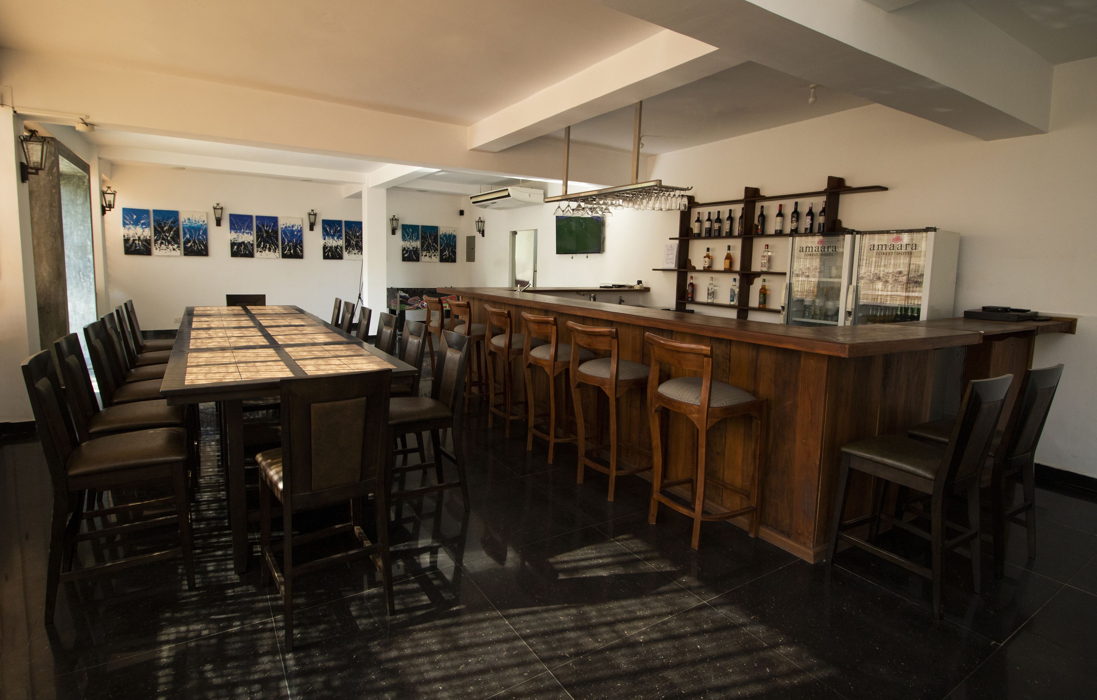 A modern bar area with a long counter, multiple stools, and a refrigerator stocked with bottles.