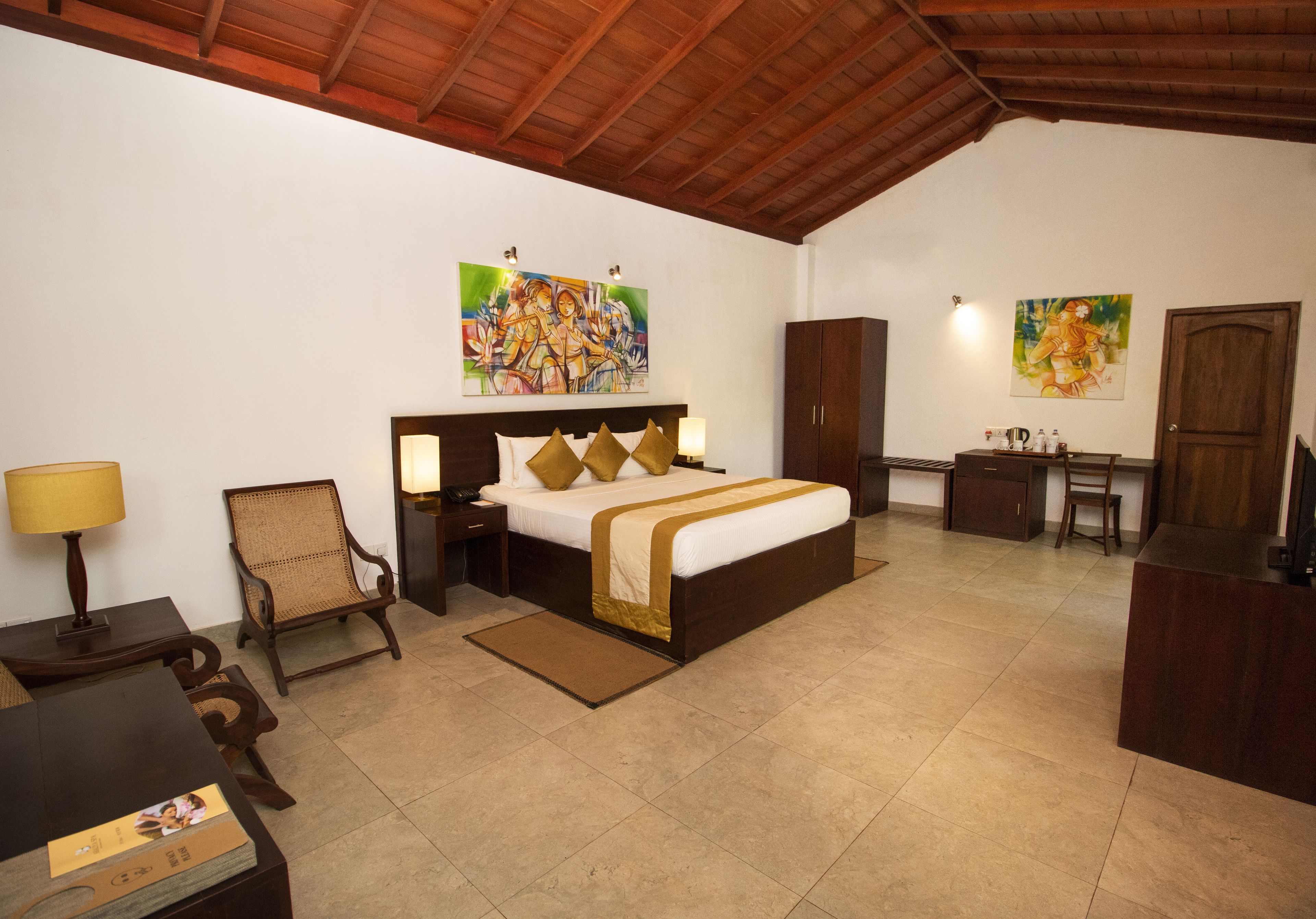 Un dormitorio con cama, mesitas de noche, una silla, escritorio y obras de arte en las paredes.