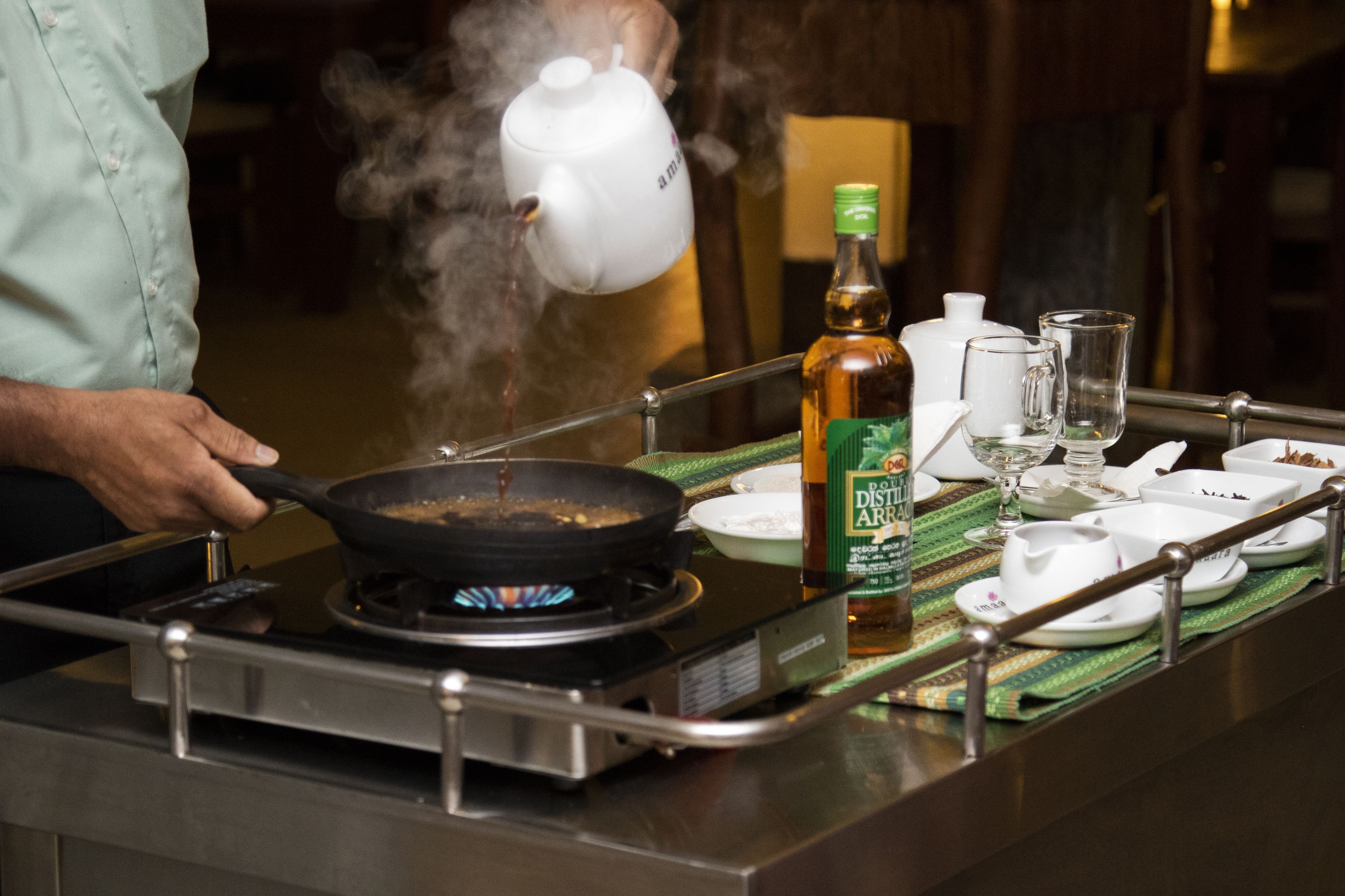A kitchen with a stove, a frying pan, a teapot, and a bottle of beer on a tray.