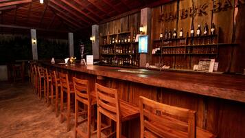 A bar with wooden chairs and shelves of bottles.