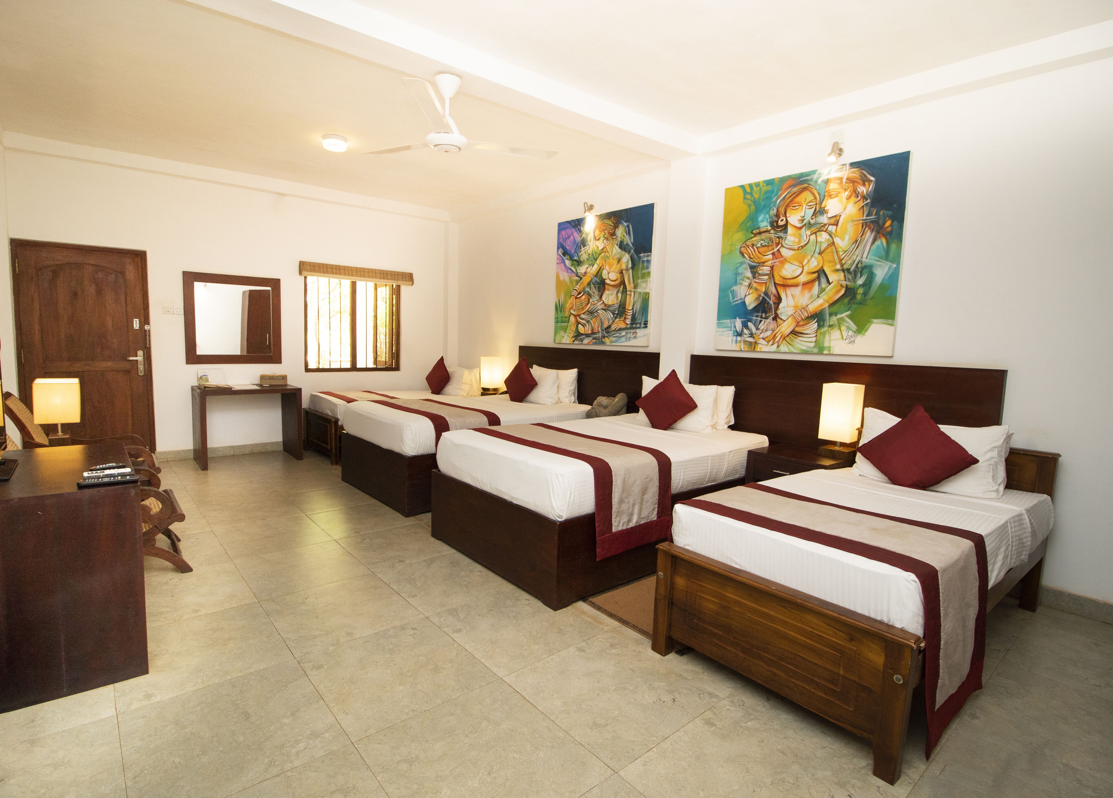 Una habitación de hotel con cuatro camas individuales, un escritorio, una silla, un espejo y obras de arte en las paredes.