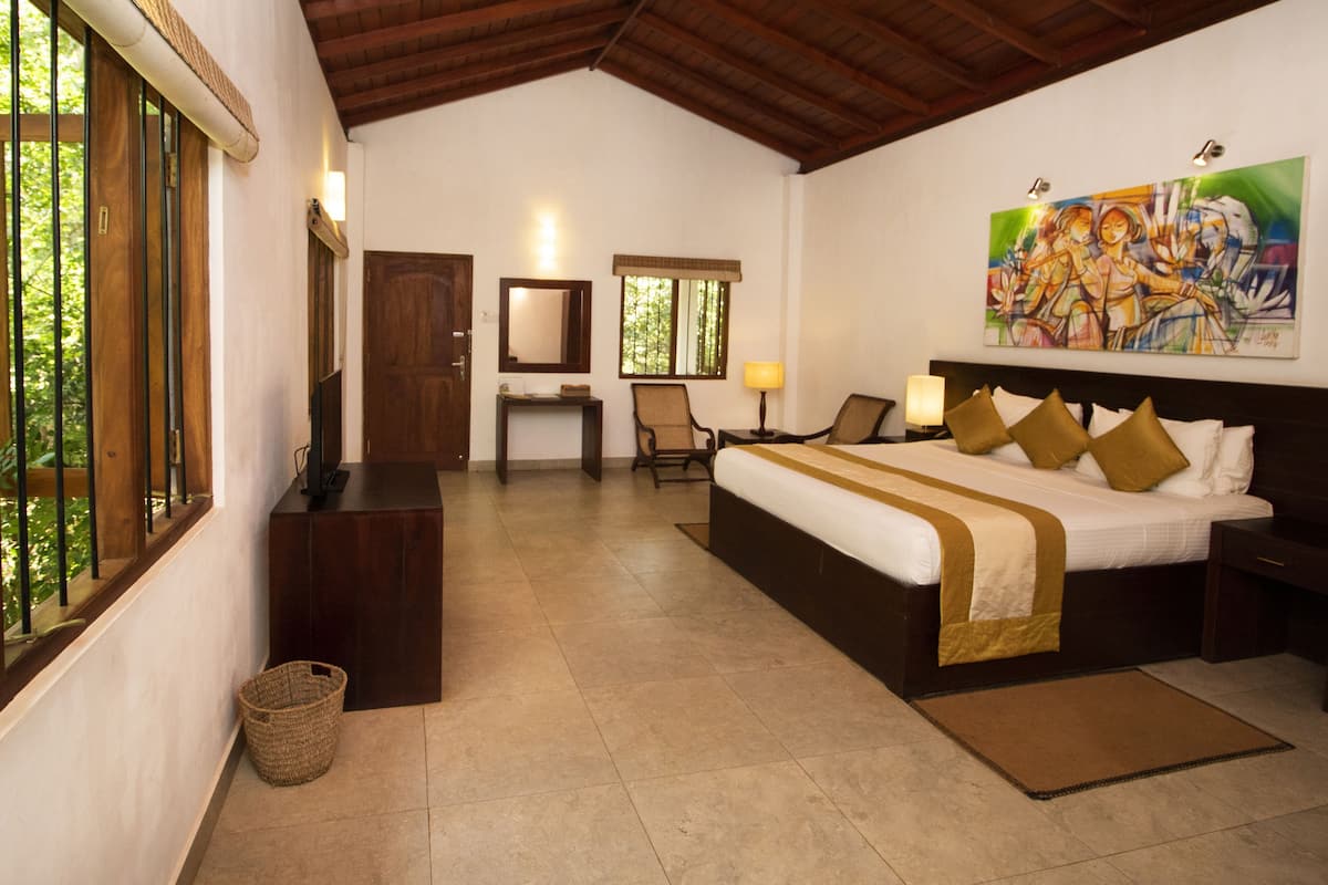 Habitación de hotel con cama, escritorio, silla, televisor, un cuadro y ventana.