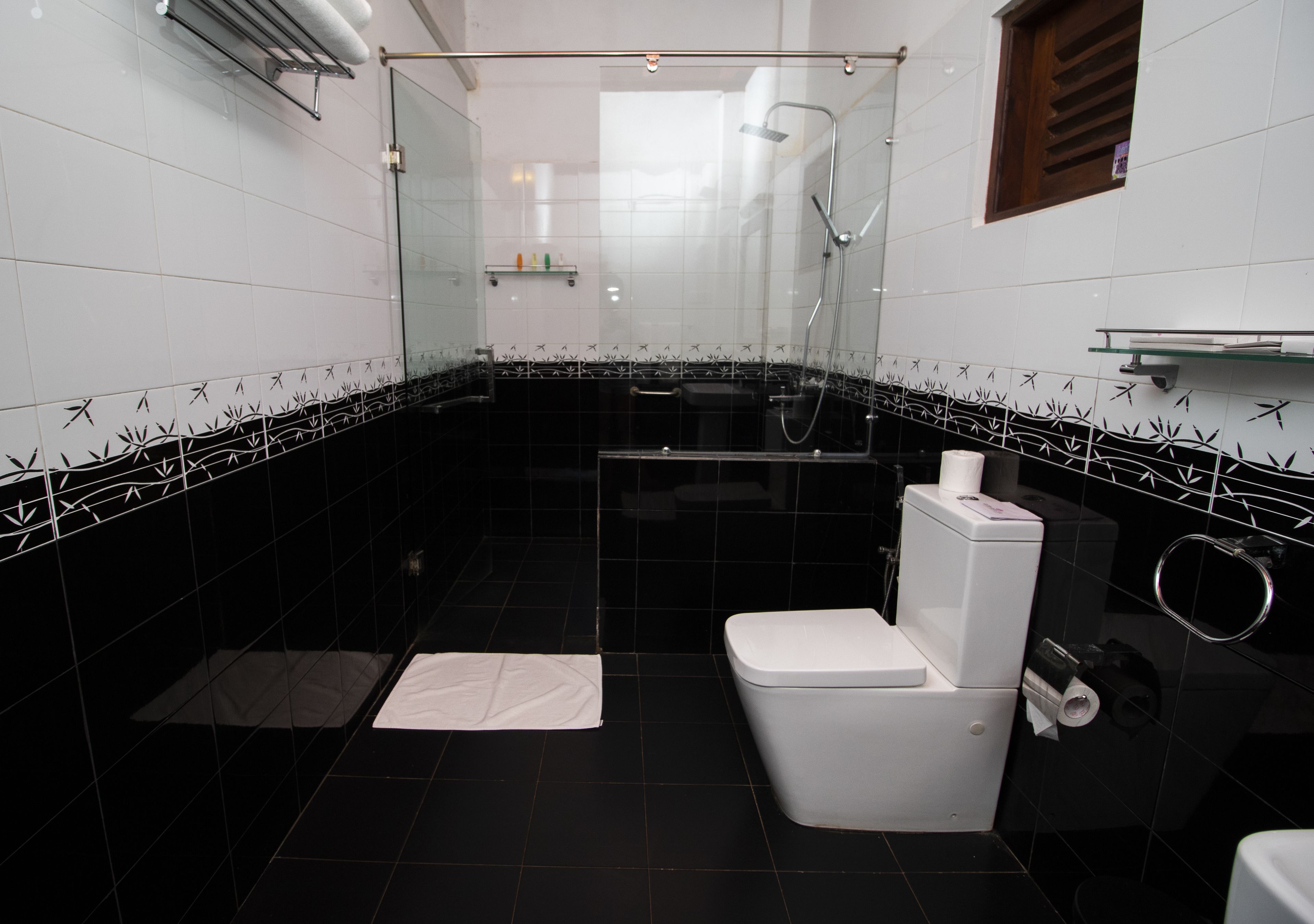 A compact bathroom with a glass-enclosed shower, a white toilet, and a small shelf with toiletries.