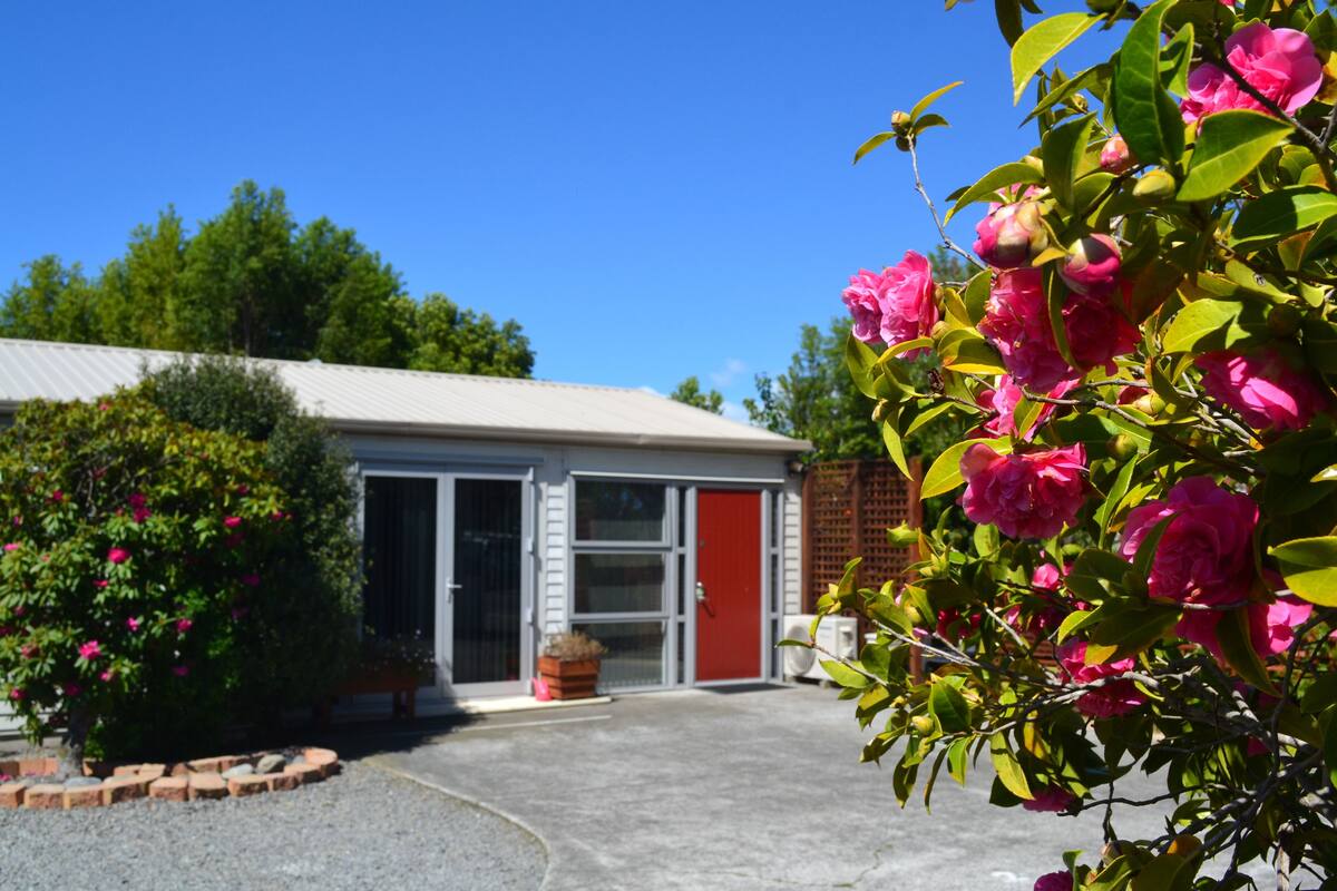 Een gebouw met een rode deur, een garage en een tuin met roze bloemen.