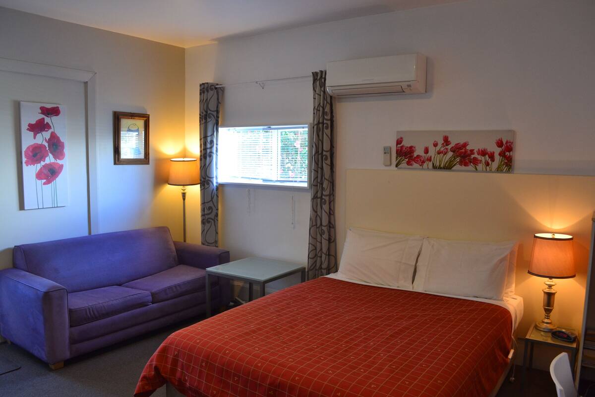 Een hotelkamer met een bed, een bank, een kleintje tafeltje en een raam met gordijnen.