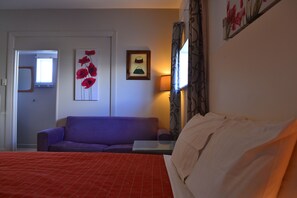 A hotel room with a bed, a purple sofa, a small table, a lamp, and artwork on the walls. - McWilliam Apartments (Christchurch)
