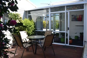A covered patio with a table and chairs, surrounded by potted plants and a view of the street. - McWilliam Apartments (Christchurch)