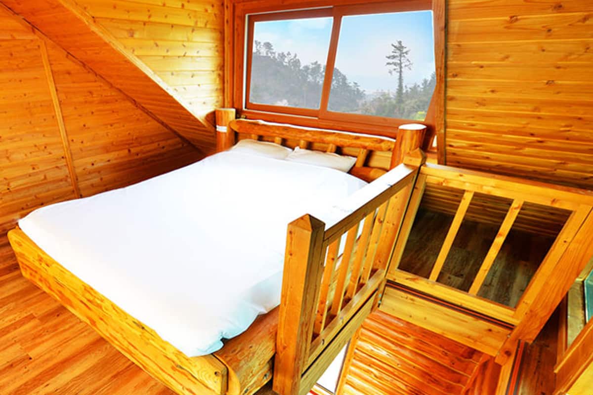 Un dormitorio de cabaña de madera con cama, ventana y cabecera de madera.