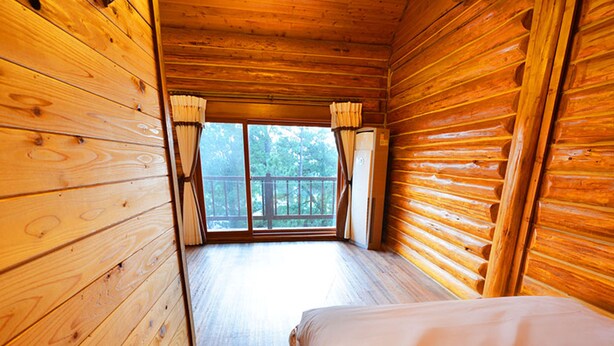 Ein Blockhauszimmer mit Holzwänden, einem Bett und einem Fenster mit Vorhängen.