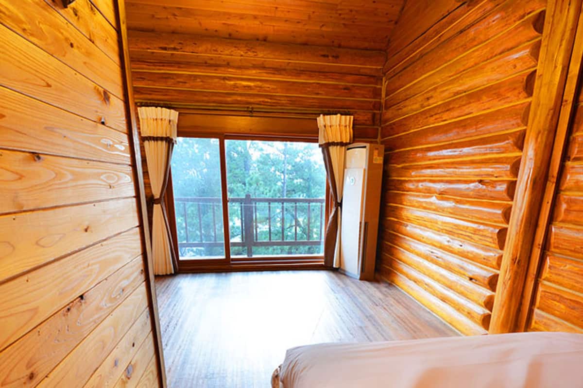 Una habitación tipo cabaña con paredes de madera, una cama y un ventanal con cortinas.