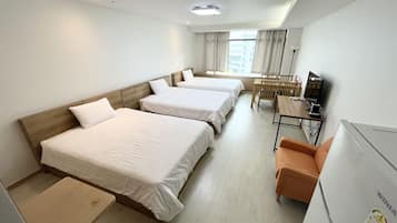Habitación de hotel con tres camas individuales, un escritorio con silla, televisión y ventana con cortinas.