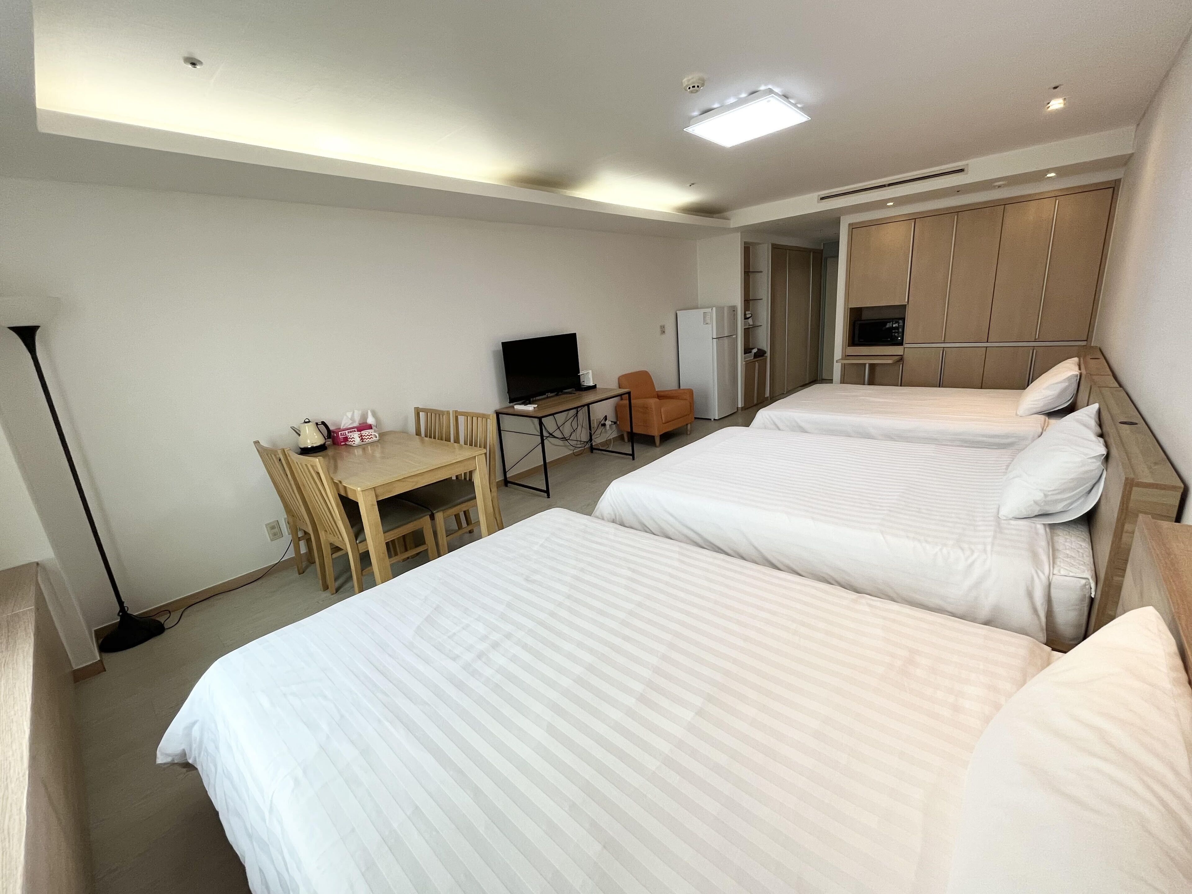 A hotel room with two beds, a desk with a chair, a television, and a wardrobe.