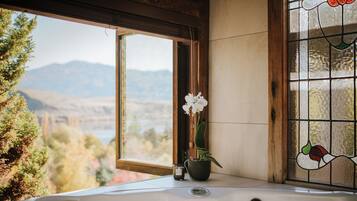 A bathroom with a bathtub, a window with a view of mountains, and a potted orchid.