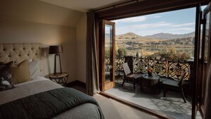 Un dormitorio con una cama grande, una mesita de noche, una lámpara y vistas a un balcón con mobiliario exterior.