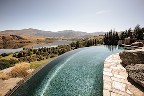 A curved infinity pool with a clear view of a lake and mountains in the background. - Stoneridge Estate (Lake Hayes)