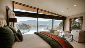 Un dormitorio con una cama grande, vistas a las montañas y un lago, y un balcón con mobiliario.