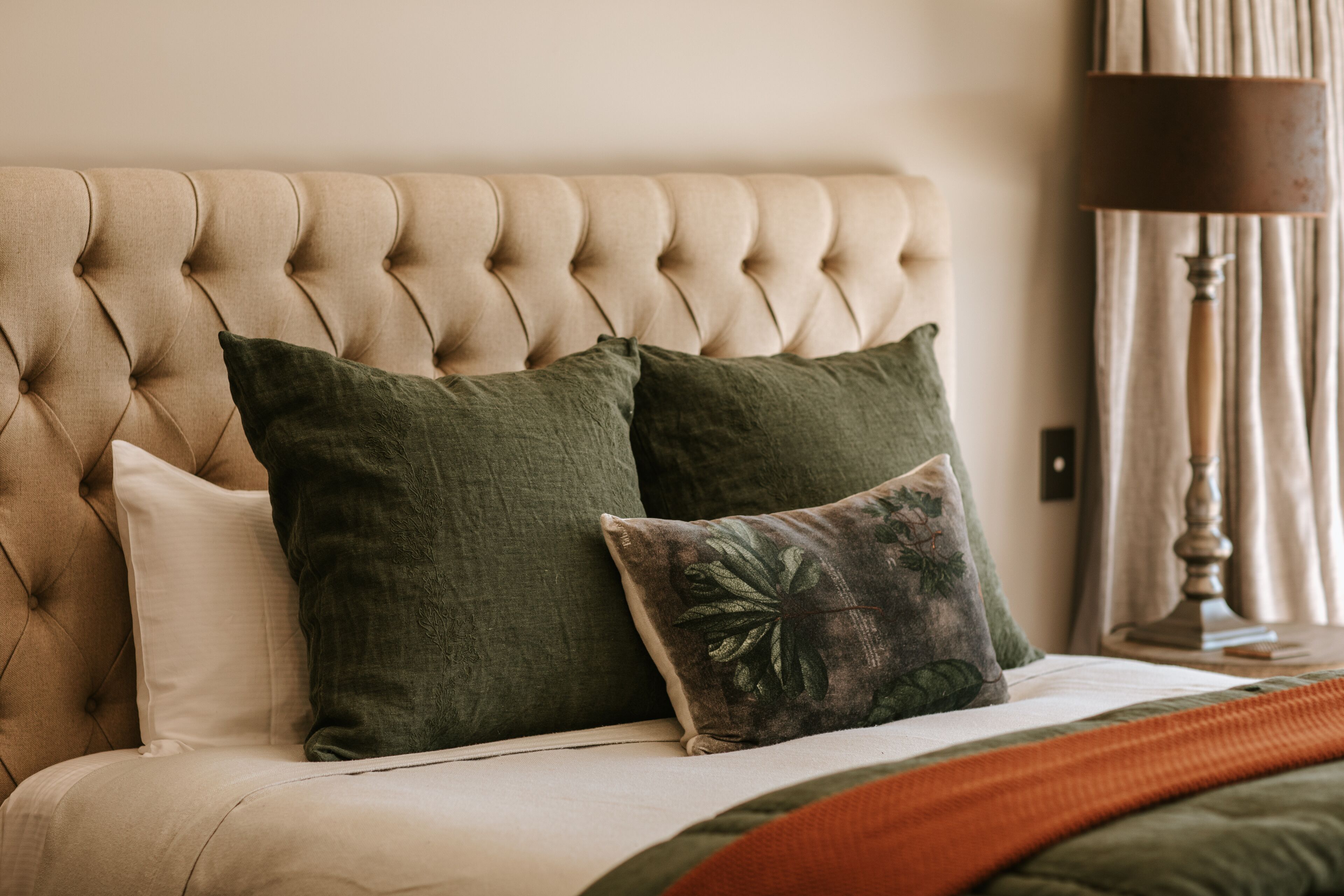Cabecera tapizada con dos almohadas verdes y una almohada decorativa con diseño de hoja.