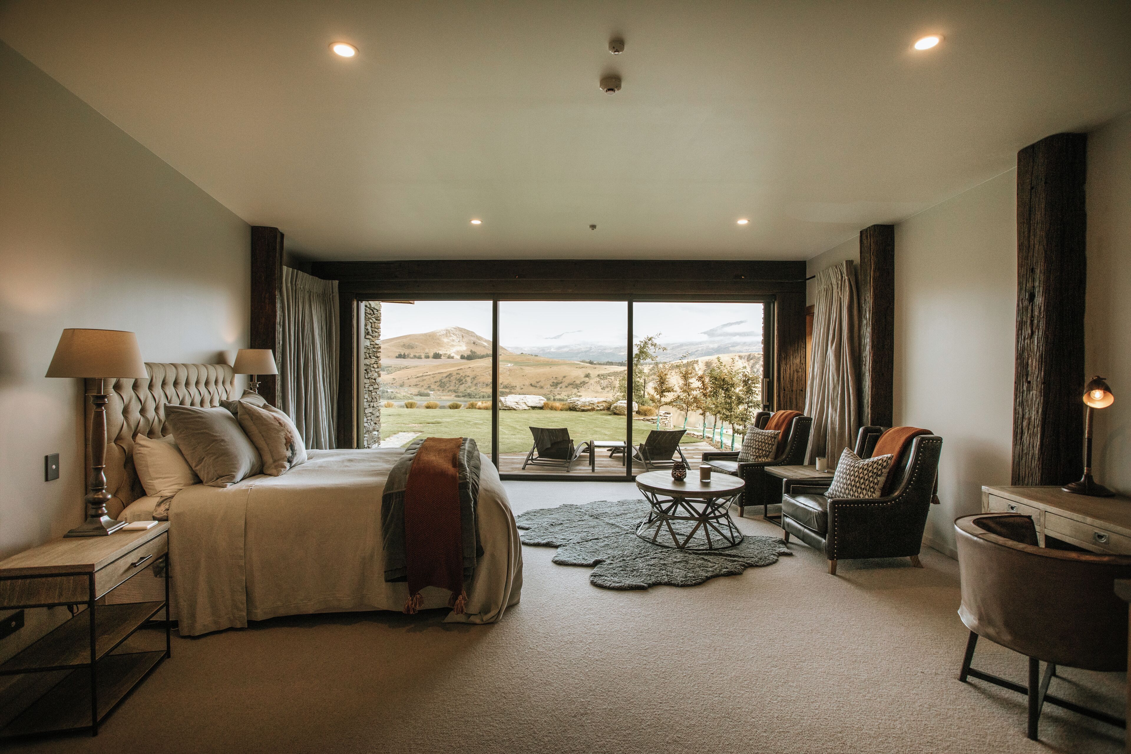 Un dormitorio amplio con una cama grande, una zona de estar con sillones, una mesita y vistas al exterior.